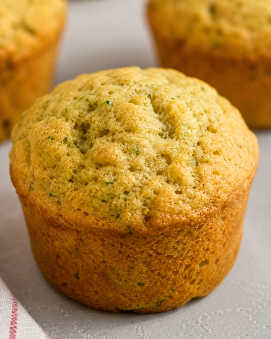 Delicious Zucchini Muffins Close-up of moist, golden zucchini muffin with background muffins on a white surface.