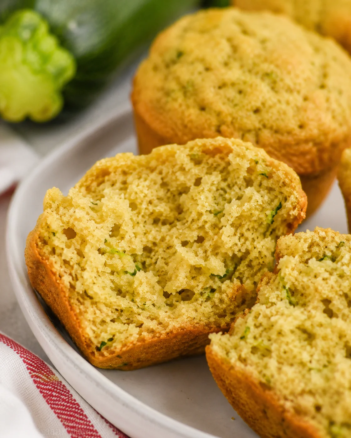Delicious Zucchini Muffins Freshly baked moist zucchini muffins on a white plate with a green vegetable in the background.