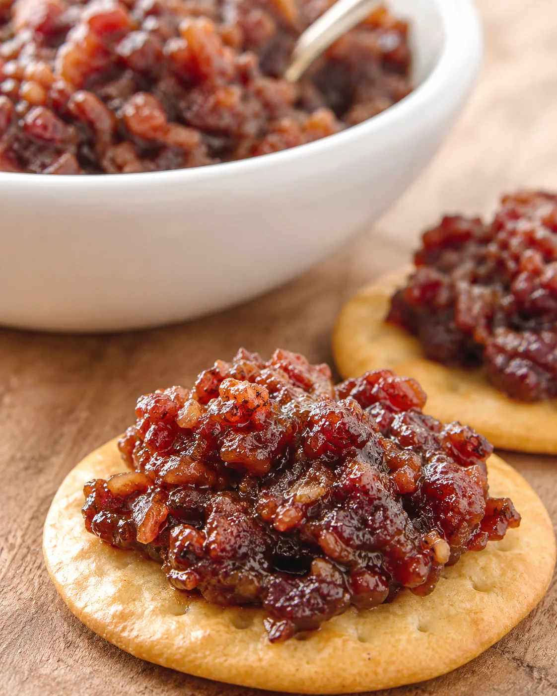 Sweet and savory bacon jam served on crackers and in a white bowl.