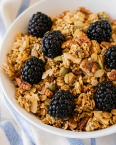 A bowl of crunchy homemade granola topped with blackberries and nuts.