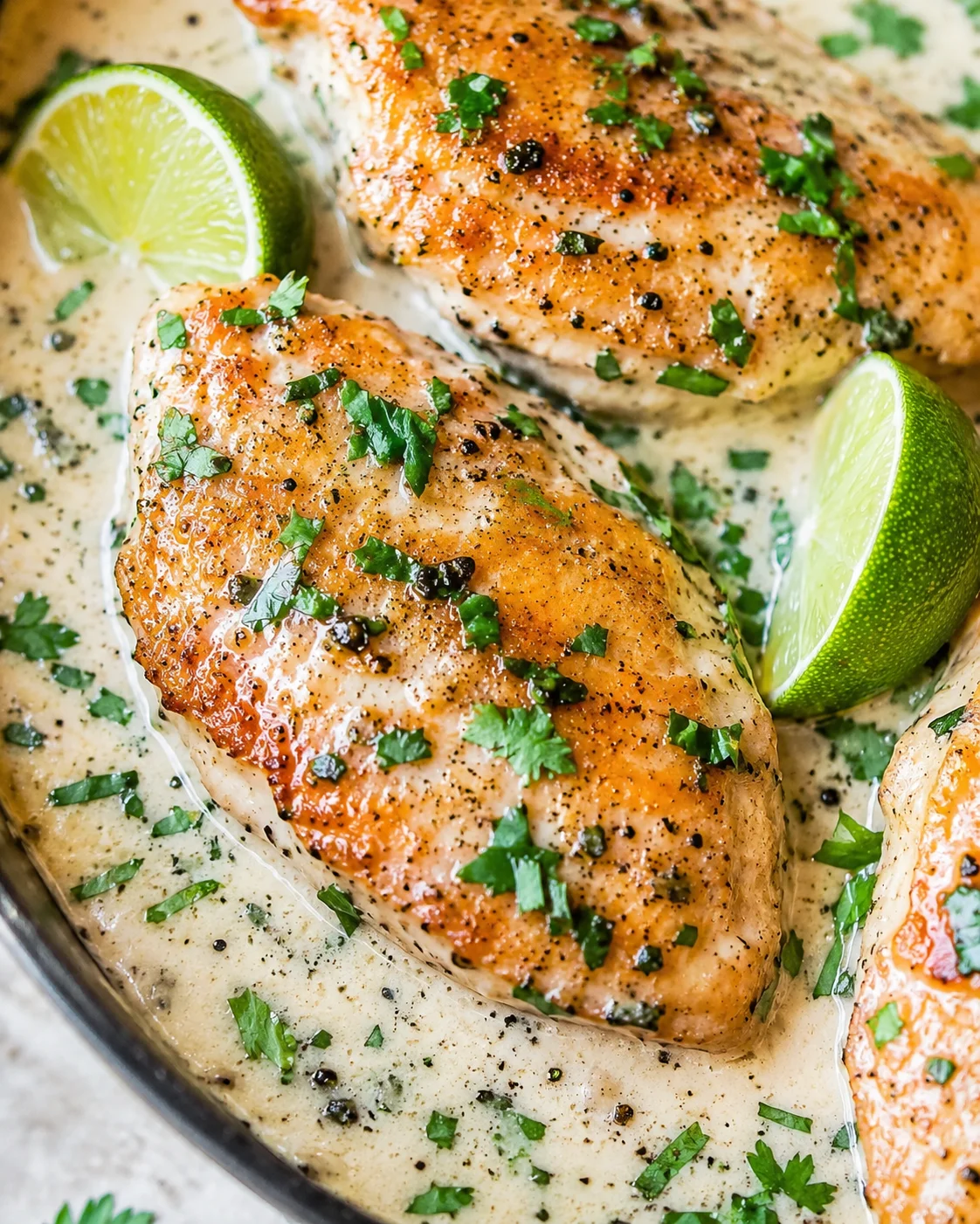 Creamy coconut lime chicken breasts in sauce garnished with cilantro and lime